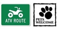 A green sign with a symbol of an ATV and "ATV Route." Next to it, a black and white sign with a paw print and text "Pets Welcome.